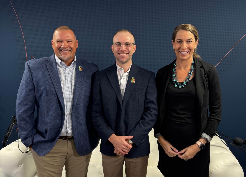 Three smiling professionals pose for a group photo in a studio, standing in front of a blue patterned backdrop.