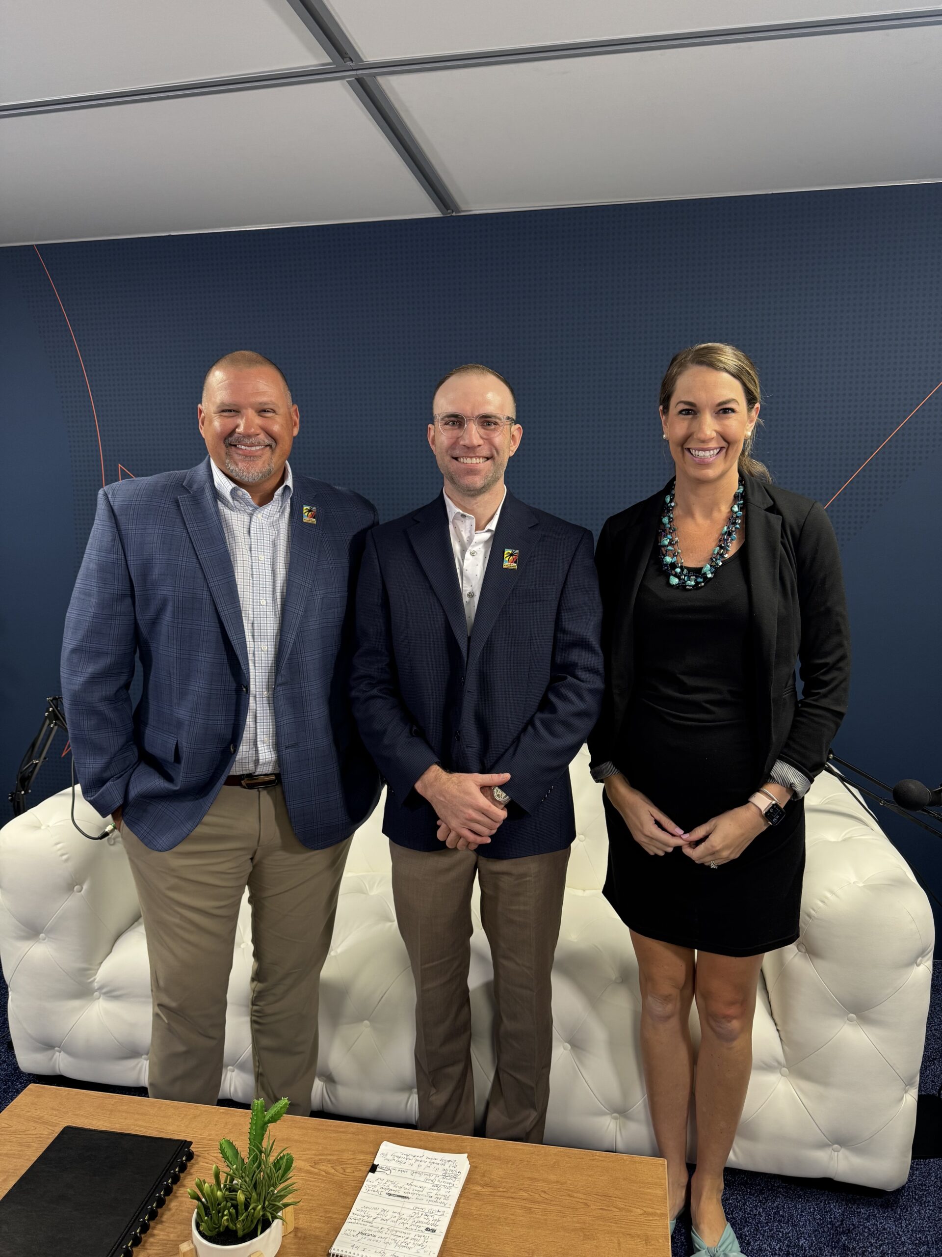 Three smiling professionals pose for a group photo in a studio, standing in front of a blue patterned backdrop.